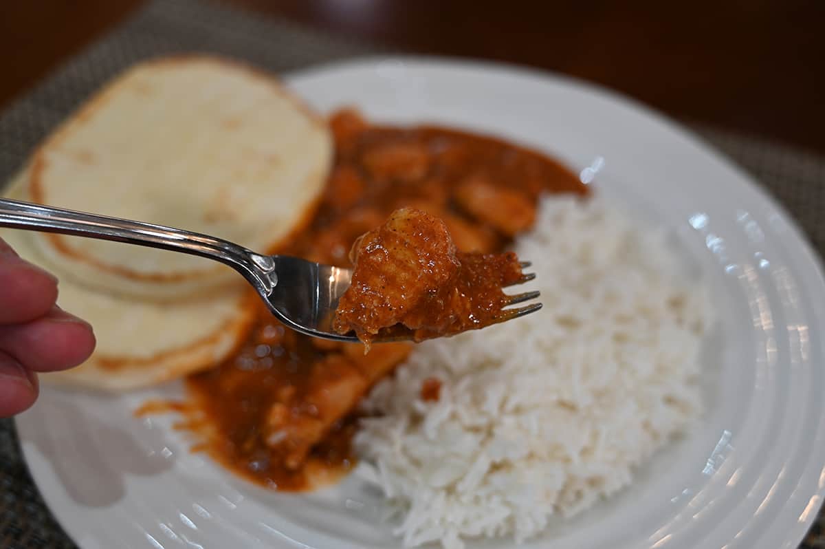 Closeup image of one forkful of vindaloo with a plate of vindaloo, rice and naan bread in the background of the image.