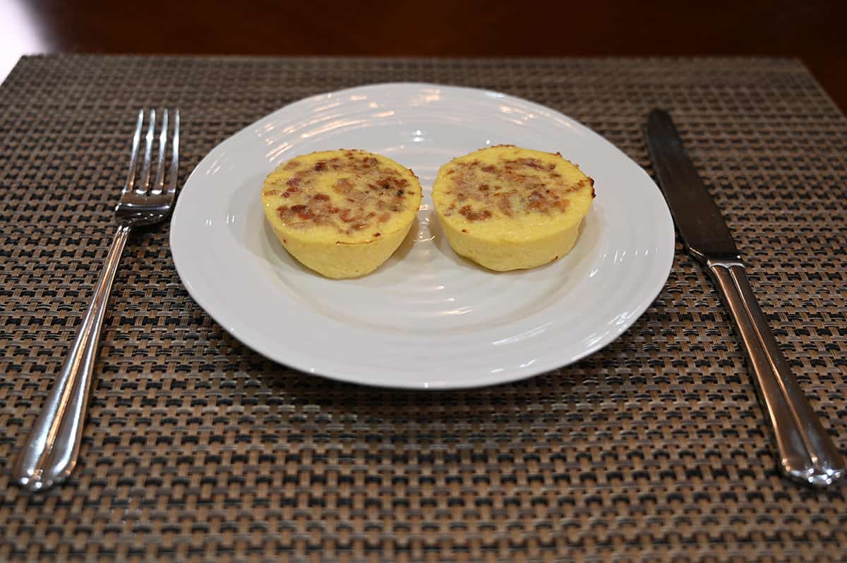 Side view image of two cooked cheese & uncured bacon egg bites sitting on a plate.