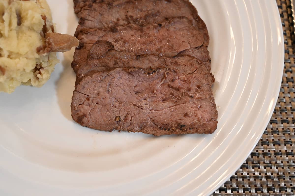 Closeup image of a few slices of cooked sirloin on a white plate, the sirloin appears 