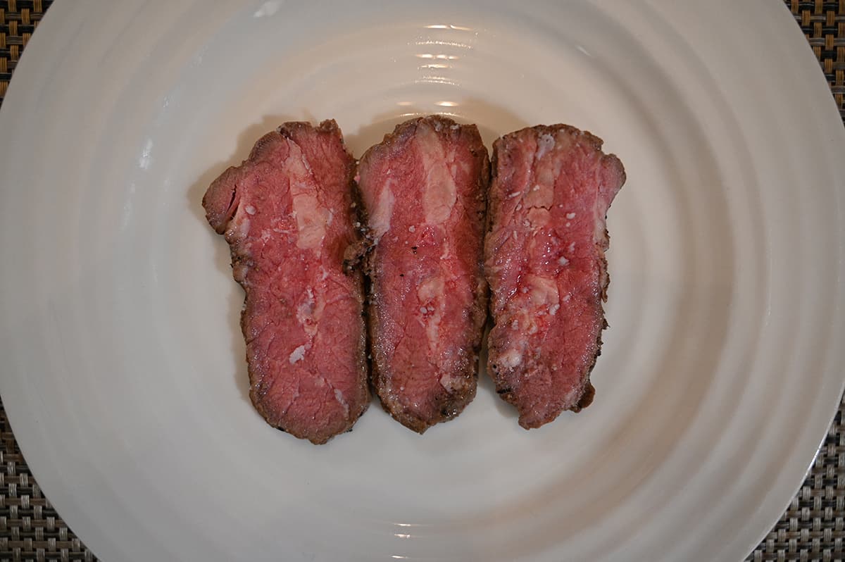 Top down image of three slices of sirloin served on a white plate, these three pieces have fat marbling throughout them.