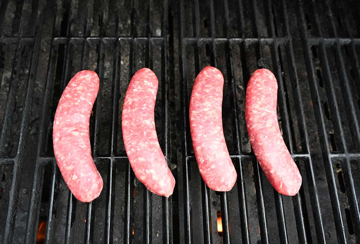 Top down image of four uncooked brats on a barbecue ready to be grilled.