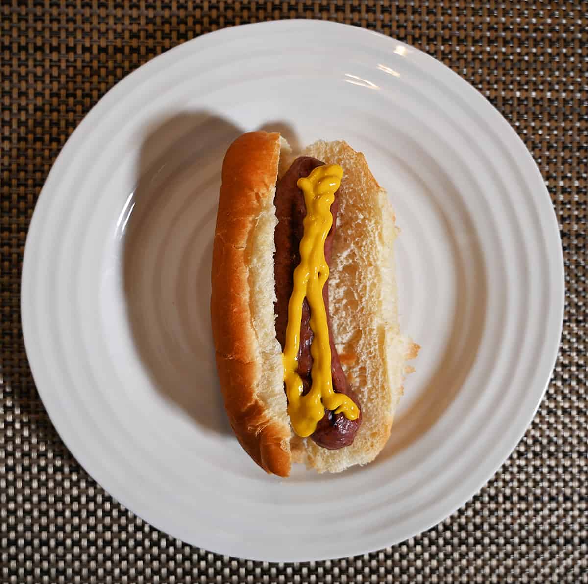 Top down image of a cooked Brat in a bun with a drizzle of mustard on top.