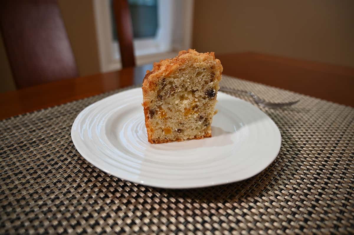 Side view image of one slice of coffee cake cut and served on a white plate with a fork beside it. You can see chunks of peach in the cake.