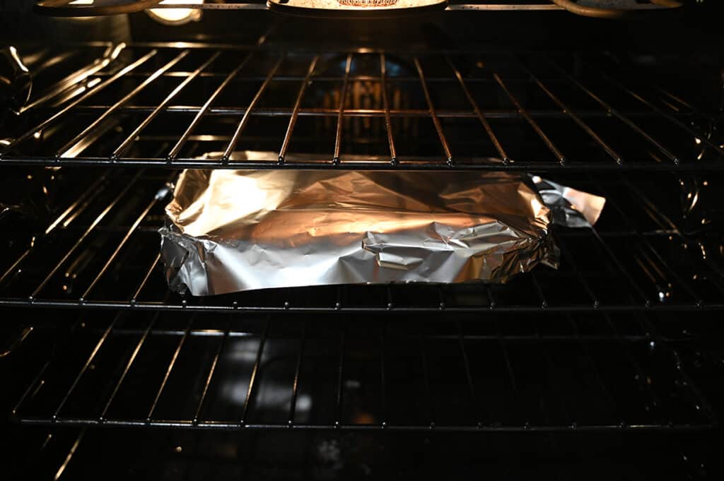 Image of the enchilada bake tray covered with foil, baking in the oven on the middle over rack.