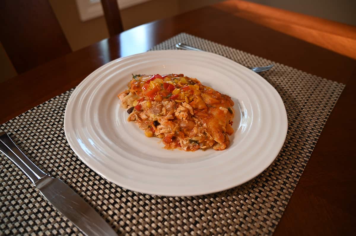 Side view image of a plate of enchilada bake showing all the various ingredients. There is a knife and fork beside the bake.