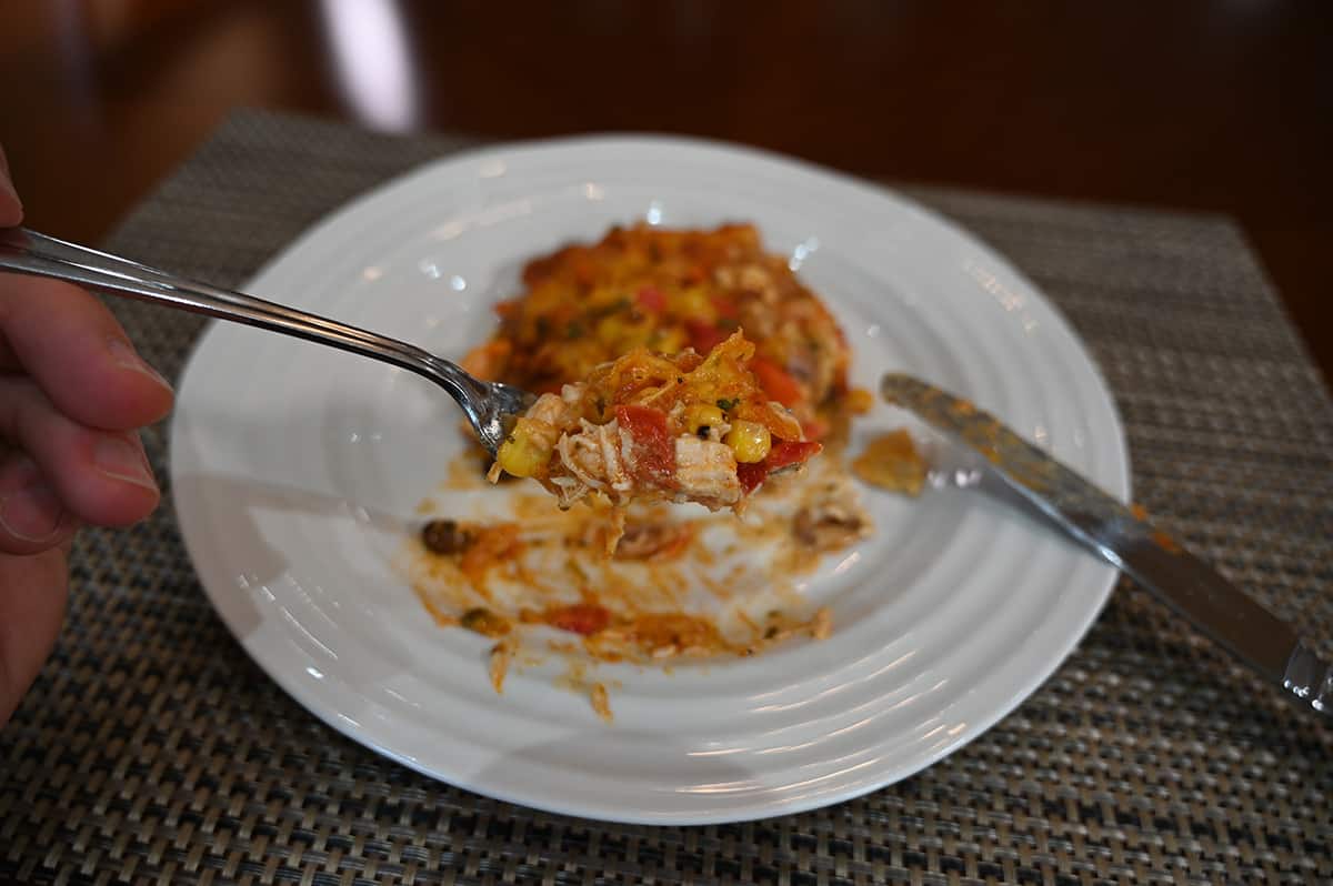 Side view closeup image of a fork close to the camera holding a bite of enchilada bake, in the background is the plate of enchilada bake.