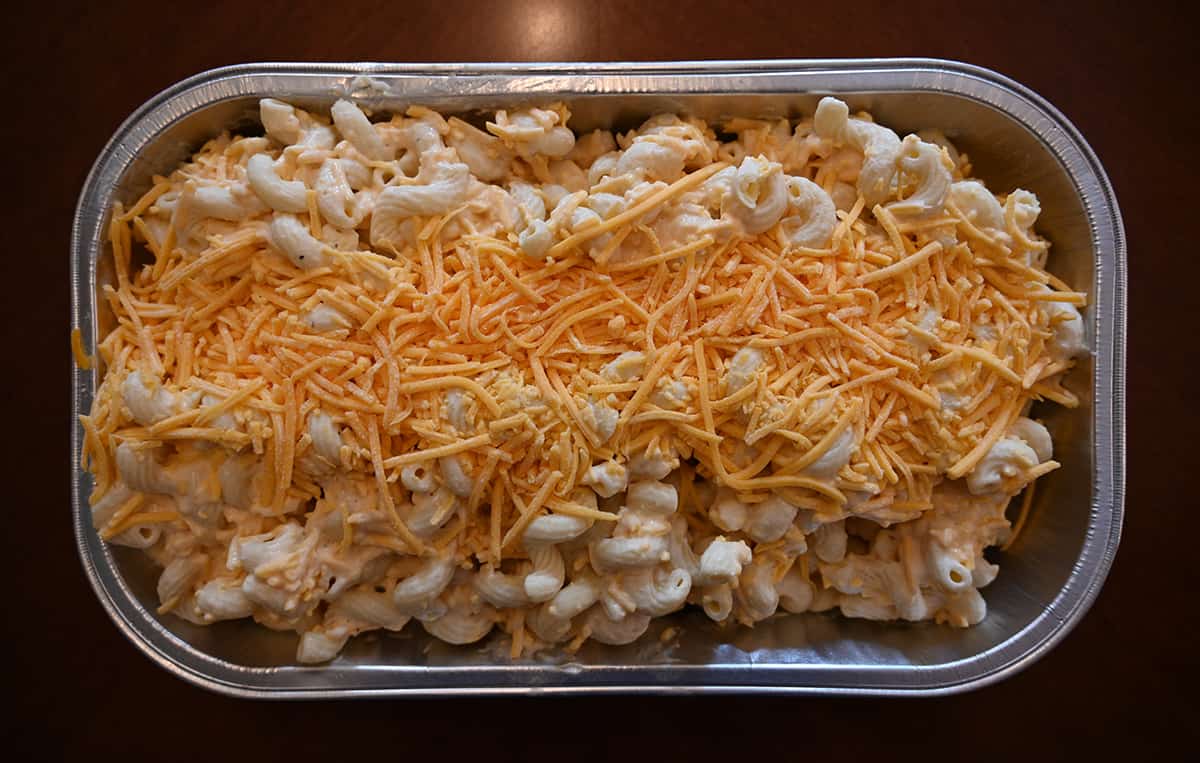 Top down image of the Costco mac and cheese unbaked with the lid off showing shredded cheese sprinkled on top.