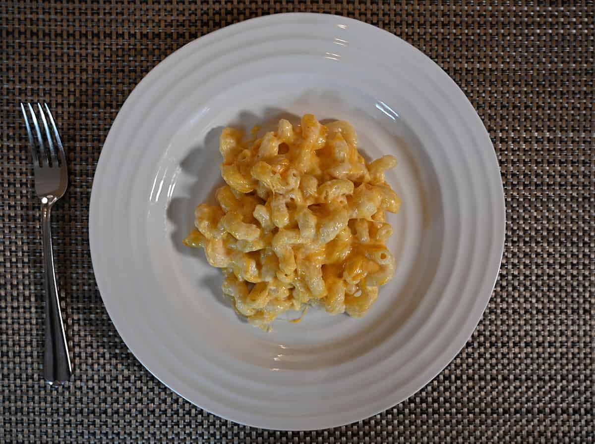 Top down image of a white plate with baked mac and cheese on it, beside the plate is a fork.