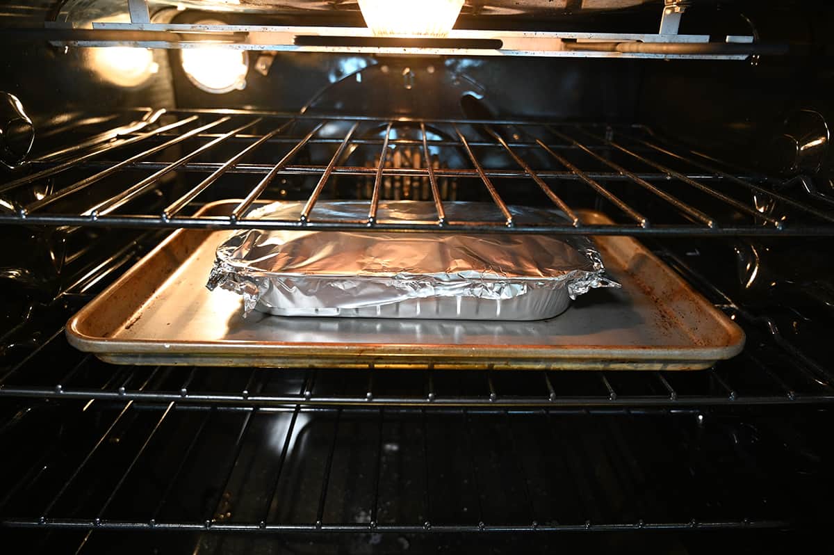 Image of the mac and cheese tray covered with foil and sitting on top of a cookie tray baking in the middle of the oven.