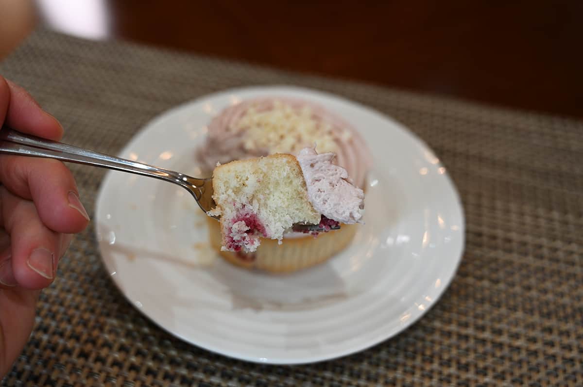 Closeup image of a fork with a bite of raspberry mini cake, in the background is a mini cake on a white plate.