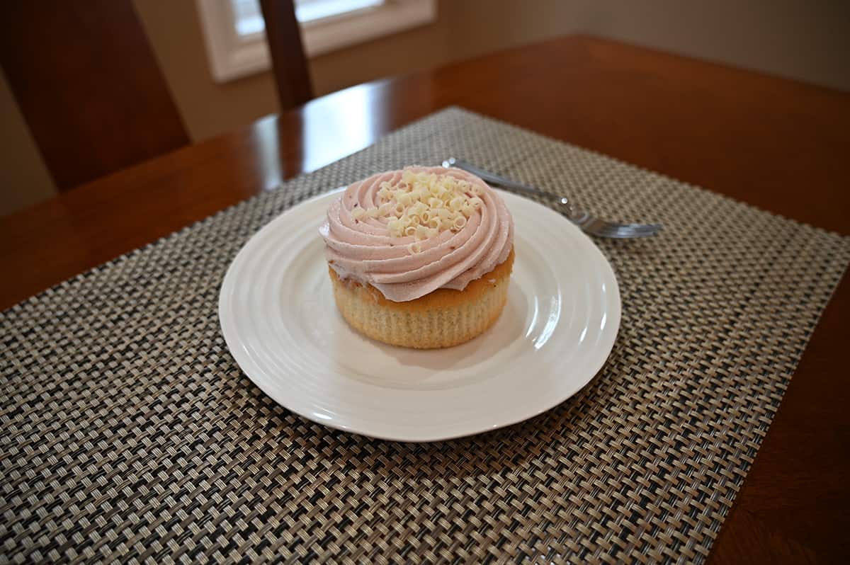 Side view image of a mini raspberry cake served on a white plate with the wrapper off.