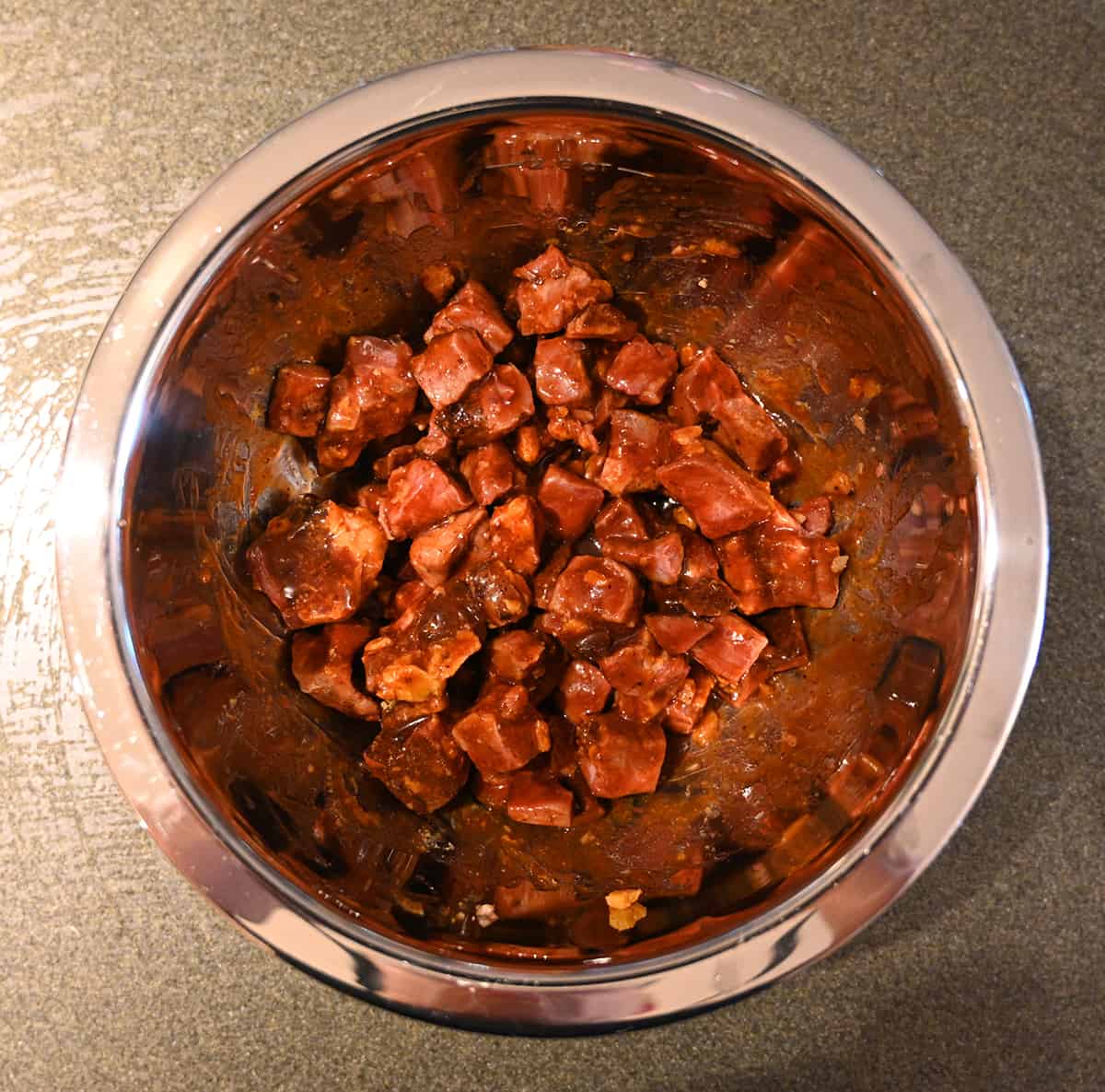 Image of a metal bowl with uncooked burnt ends in it, tossed in sauce.