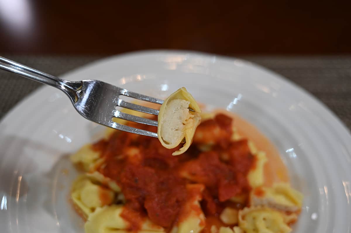 Side view closeup image of a plate of tortelloni with red sauce, a fork is holding one tortelloni with a bite taken out of it showing what the filling inside looks like.
