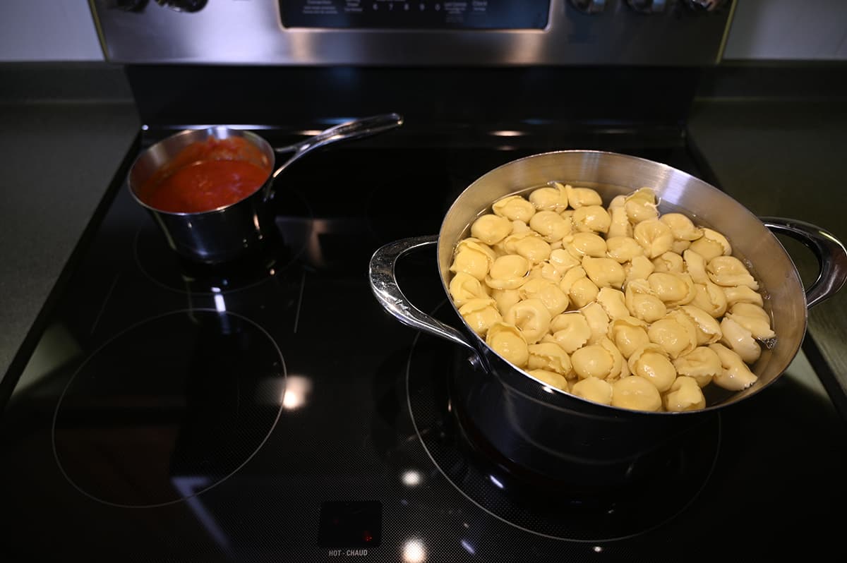 Top down image of a pot of boiling water with tortelloni in it on a stovetop and beside it is a pot of red sauce cooking.