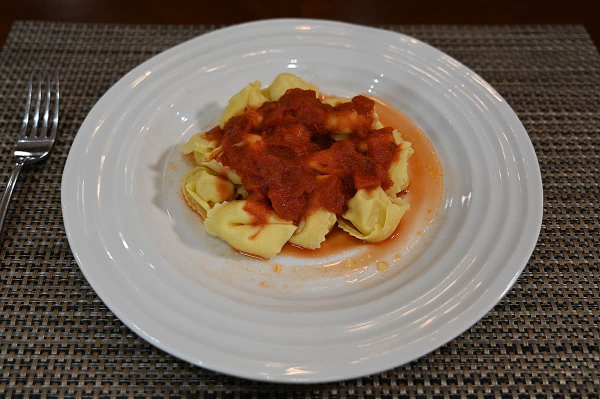 Side view image of the tortelloni cooked and prepared, served on a white plate with a red sauce.