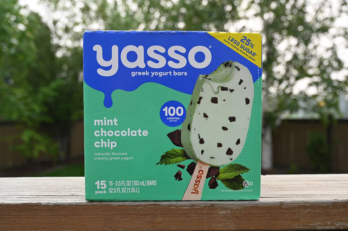 Costco Yasso Greek Yogurt Bars box sitting on a deck ledge outside with trees in the background.
