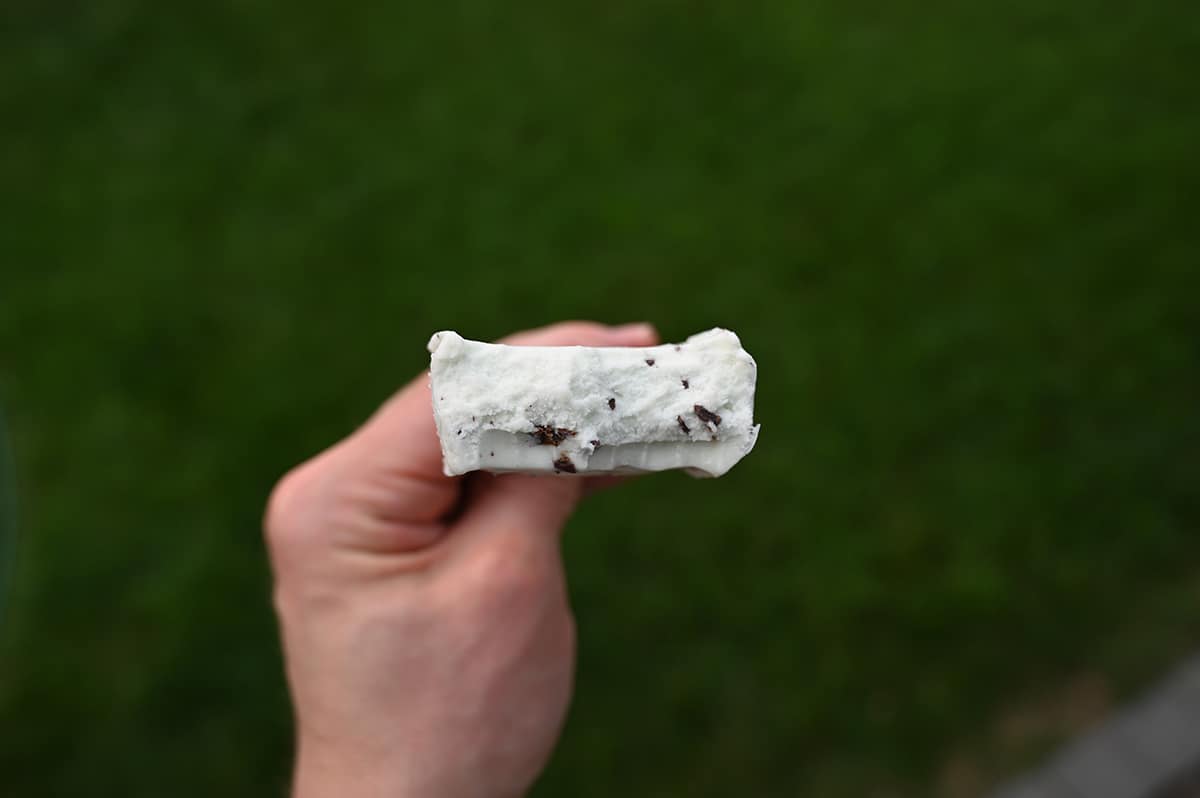 Closeup image of a hand holding one Yasso bar with a few bites taken out of it so you can see the center.