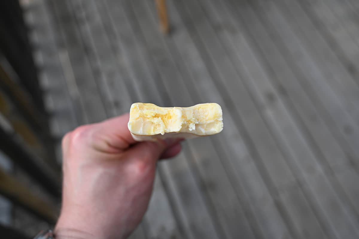 Closeup image of a hand holding one mango flavored bar with a bite taken out of it so you can see the center.