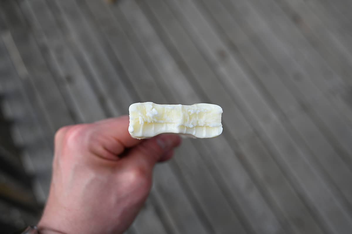 Closeup image of a hand holding one coconut flavored bar with a bite taken out of it so you can see the center.