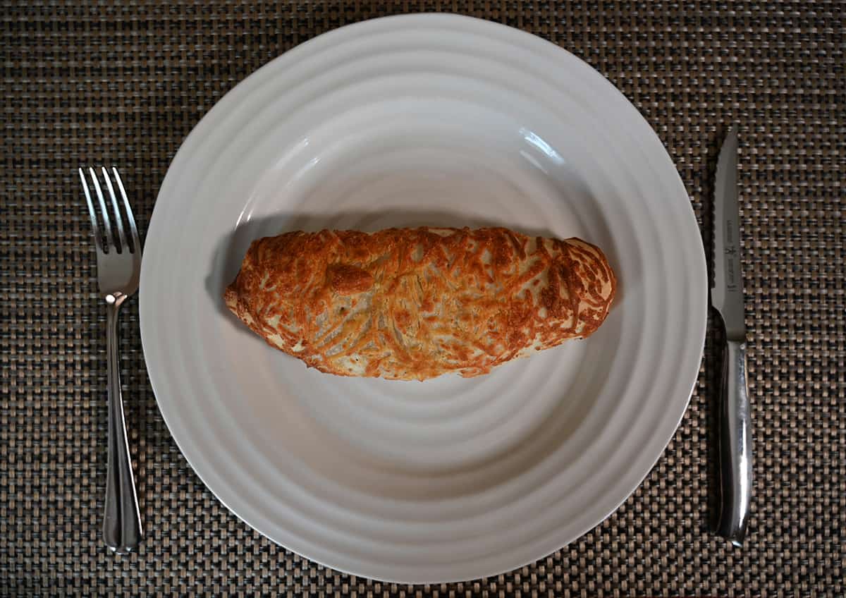 Top down image of the Costco Kirkland Signature Chicken Bake baked and served on a white plate. There is a fork and knife beside the plate.