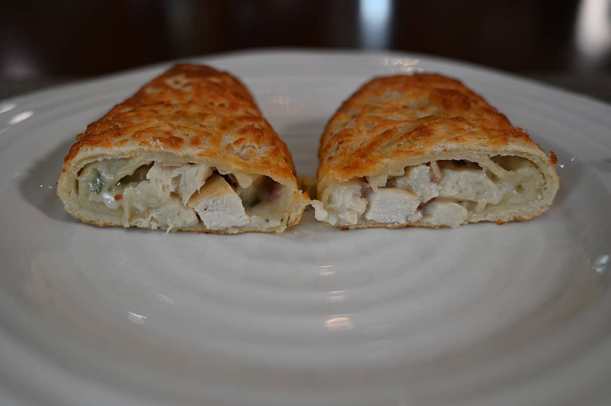 Sideview image of one chicken bake cut open on a white plate so you can see the inside. The filling is mostly chicken.