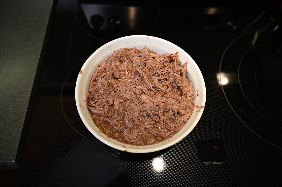 Image of the beef pot roast cooked and pulled apart, it is served in the microwave safe dish.