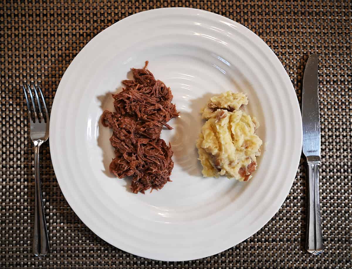 Top down image of a white plate with beef pot roast beside a heap of mashed potatoes.