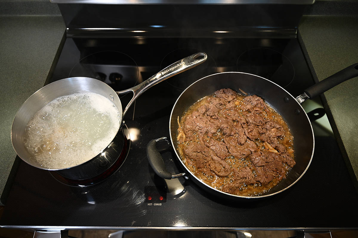 Top down image of cooked beef bulgogi in a frying pan beside a boiling pot of water with noodles in it.