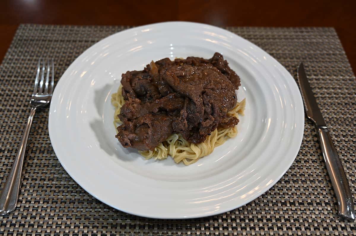 Side view image of a plate of cooked beef bulgogi served on top of some noodles.