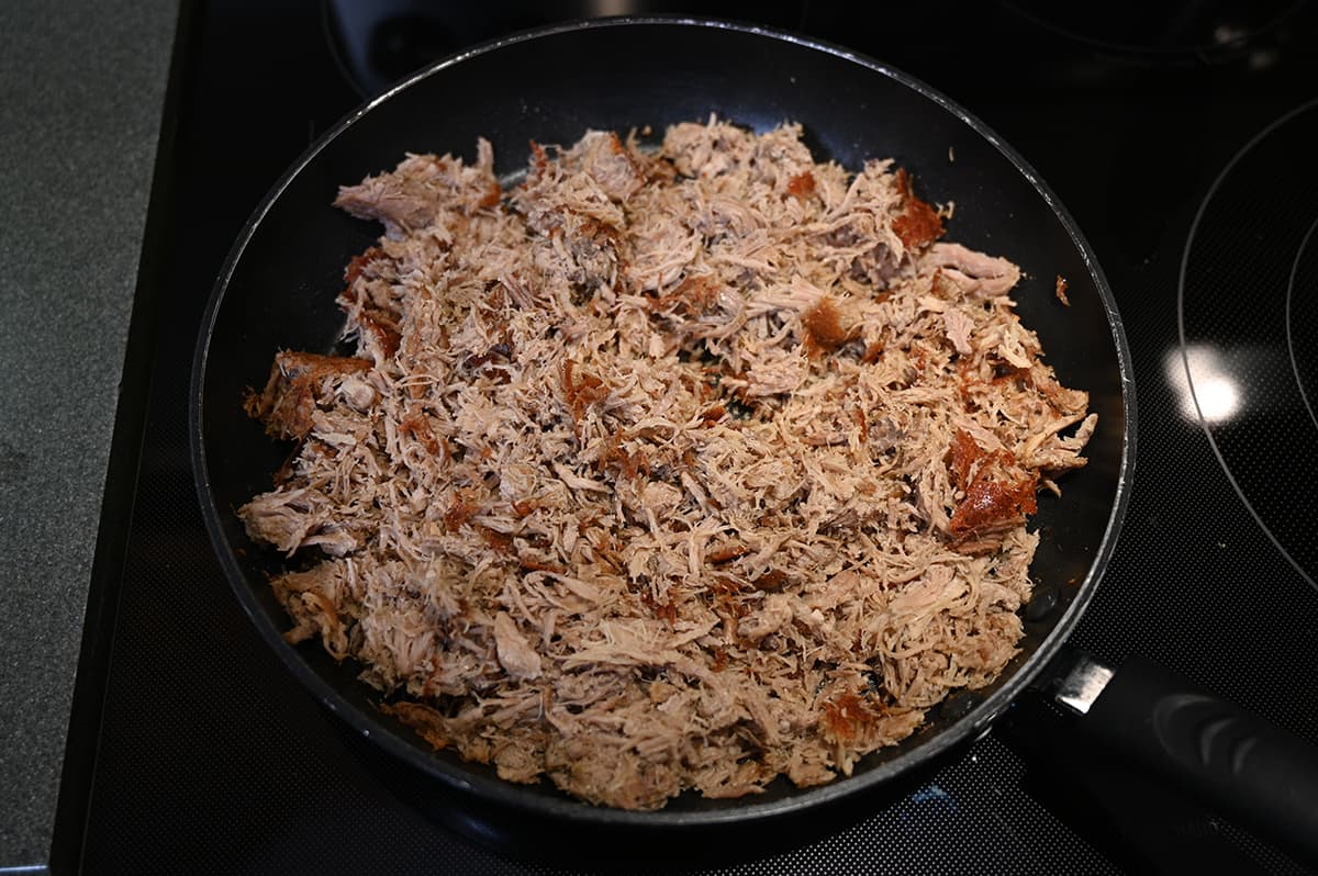 Top down image of a pan on a stovetop with cooked pork carnitas. The carnitas appear slightly crispy.