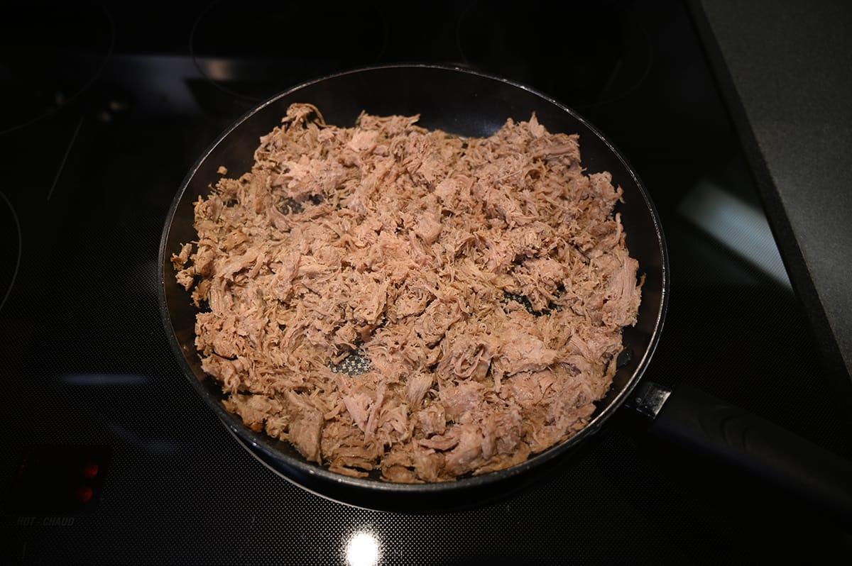 Top down image of a pan on the stove with cooked pork carnitas in it, the pork is not crisped up yet.