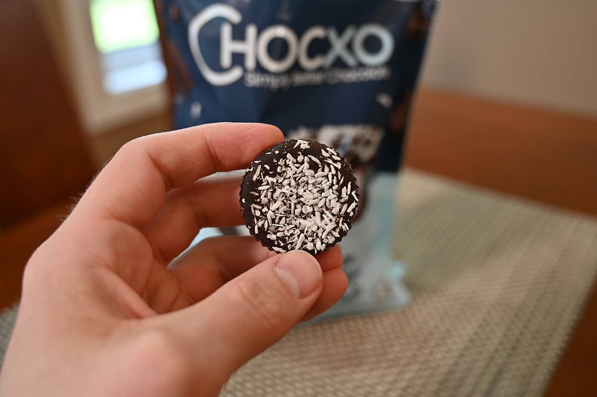 Image of a hand holding one coconut cup unwrapped close to the camera. 