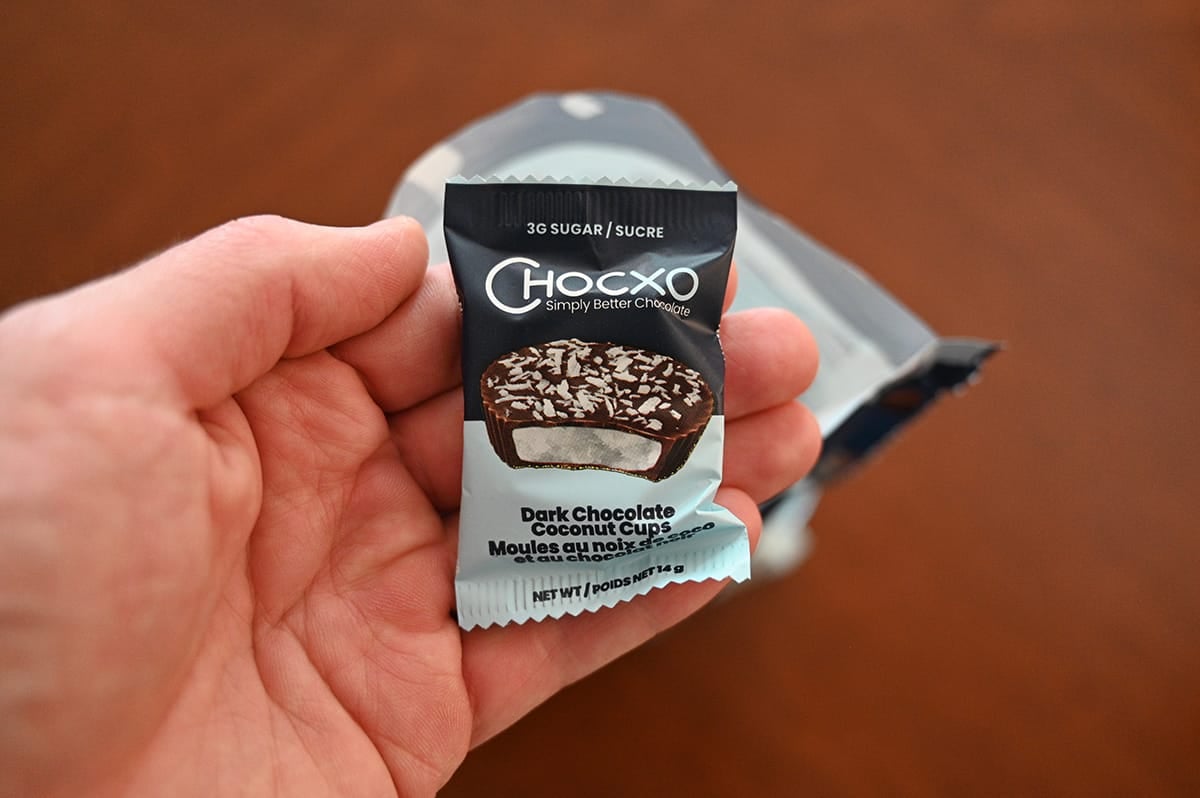 Closeup image of a hand holding one individually packaged coconut cup close to the camera.