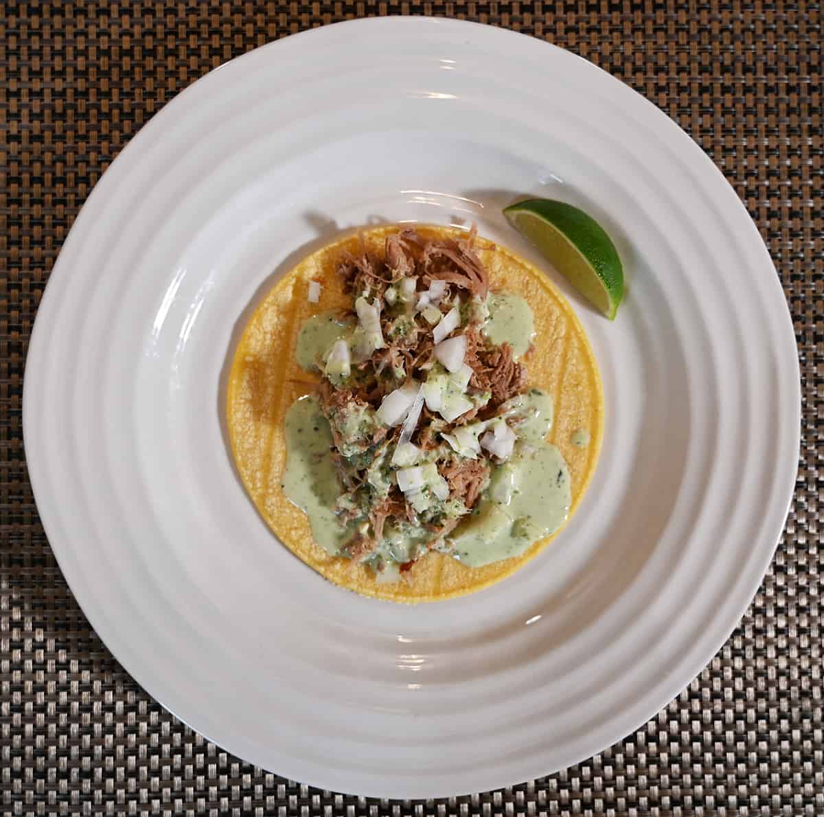 Top down image of a corn tortilla with pork on it. On the pork there is drizzled crema.