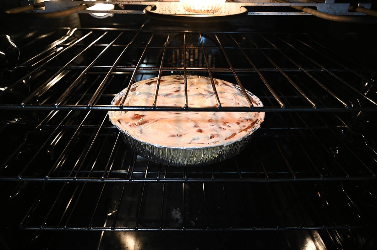 Image of the aluminum container of cinnamon rolls in an oven on the middle rack baking. 