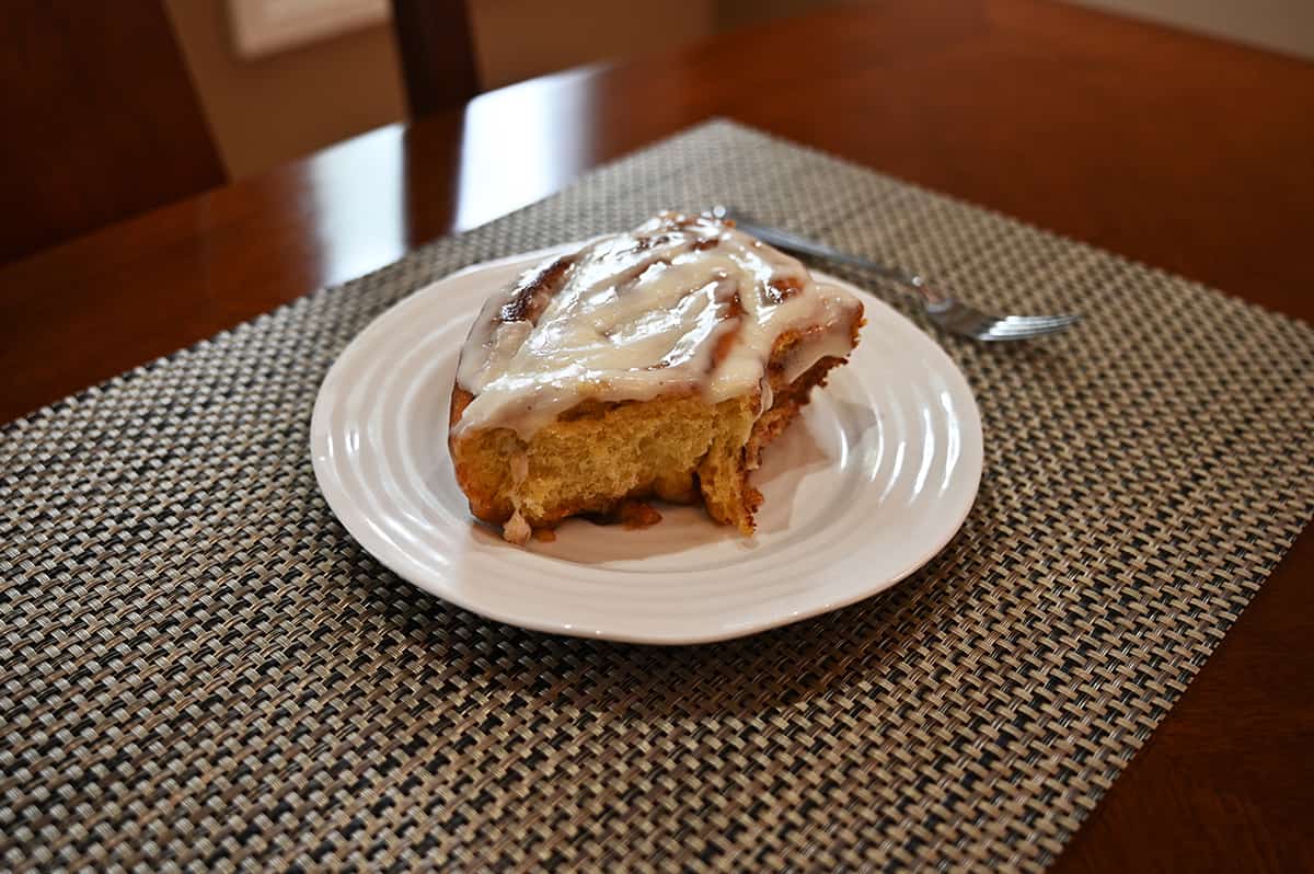 Top down image of one cinnamon roll served on a white plate, the icing is melted from being heated.