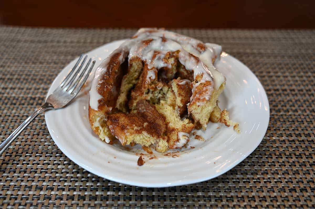 Closeup side view image of one cinnamon roll served on a white plate with a bites taken out of it so you can see the inside.