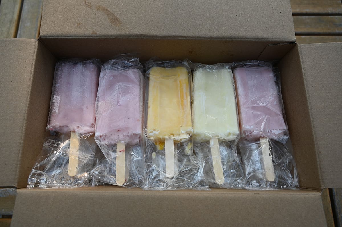 Top down image of the open box of ice cream bars showing the bars individually wrapped and all three flavors, mango, strawberry and coconut.
