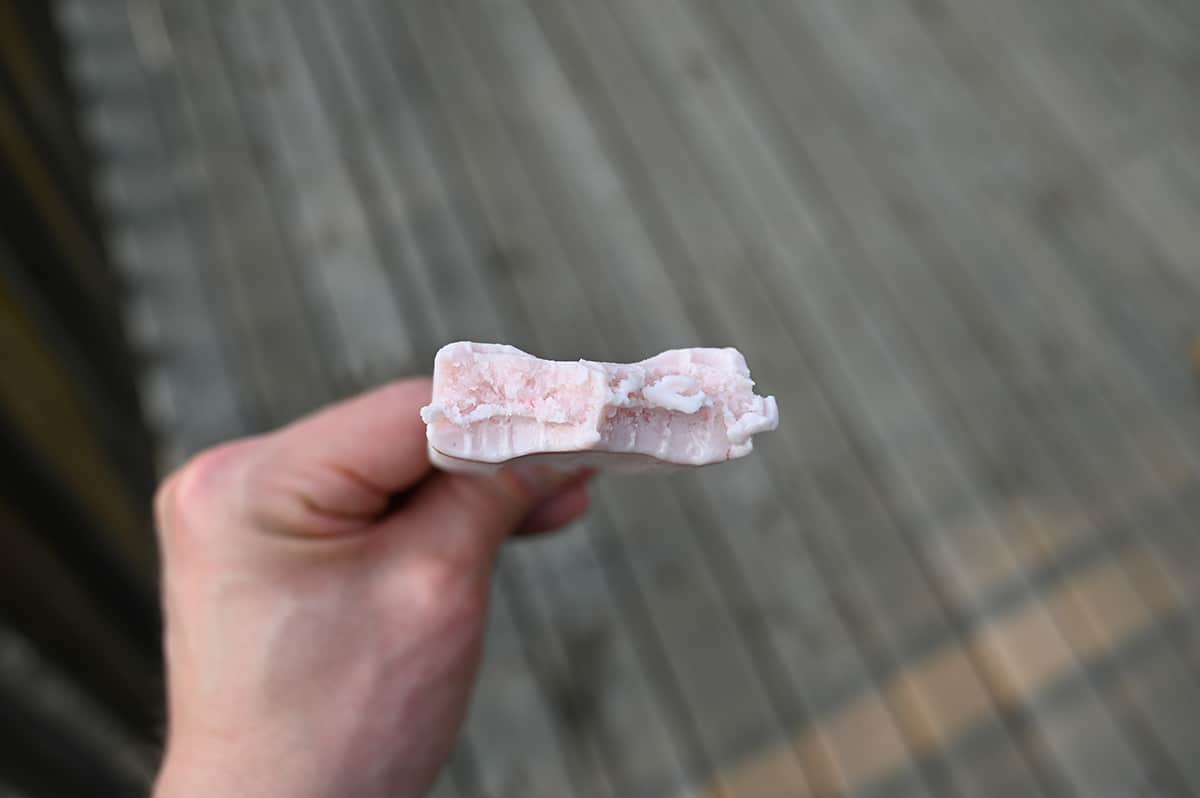 Closeup image of a hand holding one strawberry flavored bar with a bite taken out of it so you can see the center.