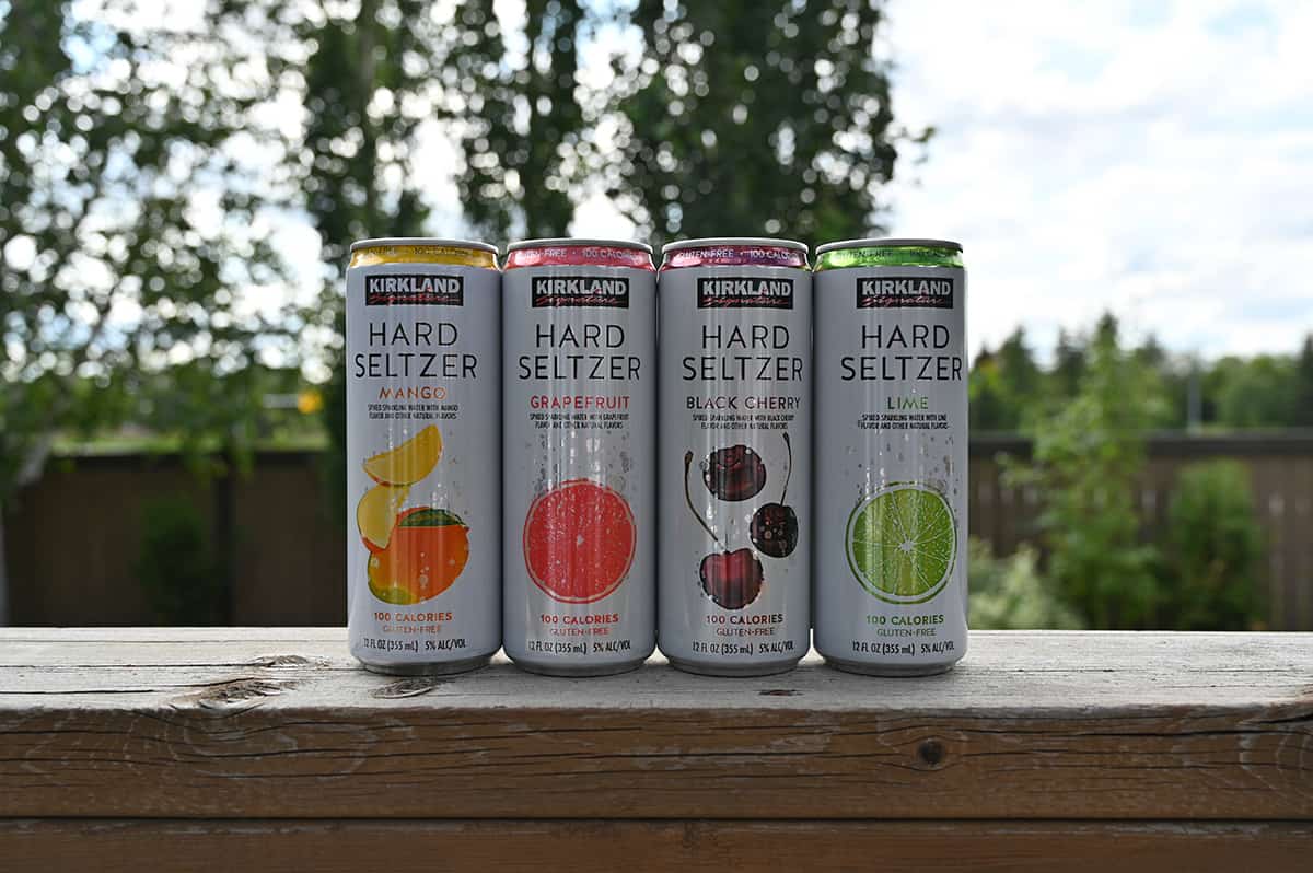 Image of the four cans of hard seltzer sitting on a deck with trees in the background. There is one can of each flavor of hard seltzer. 