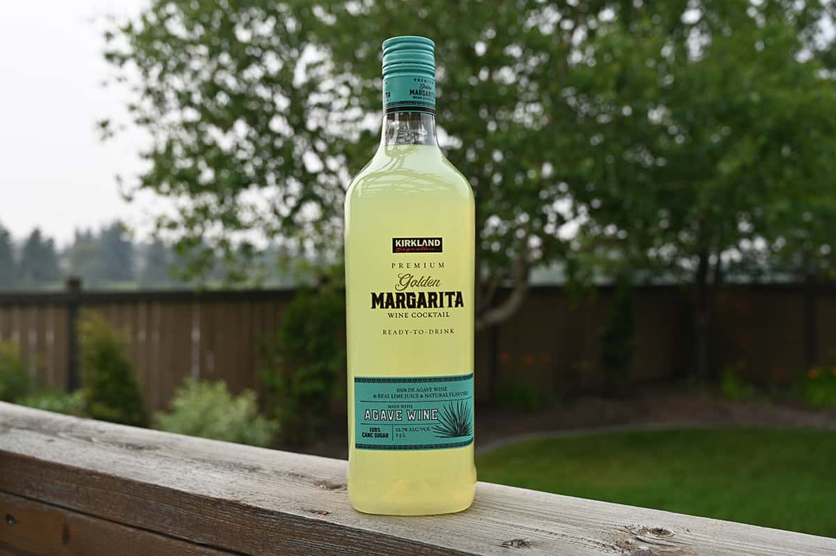 Image of the Kirkland Signature Premium Golden Margarita Wine Cocktail standing on a deck with trees, grass and a fence in the background.