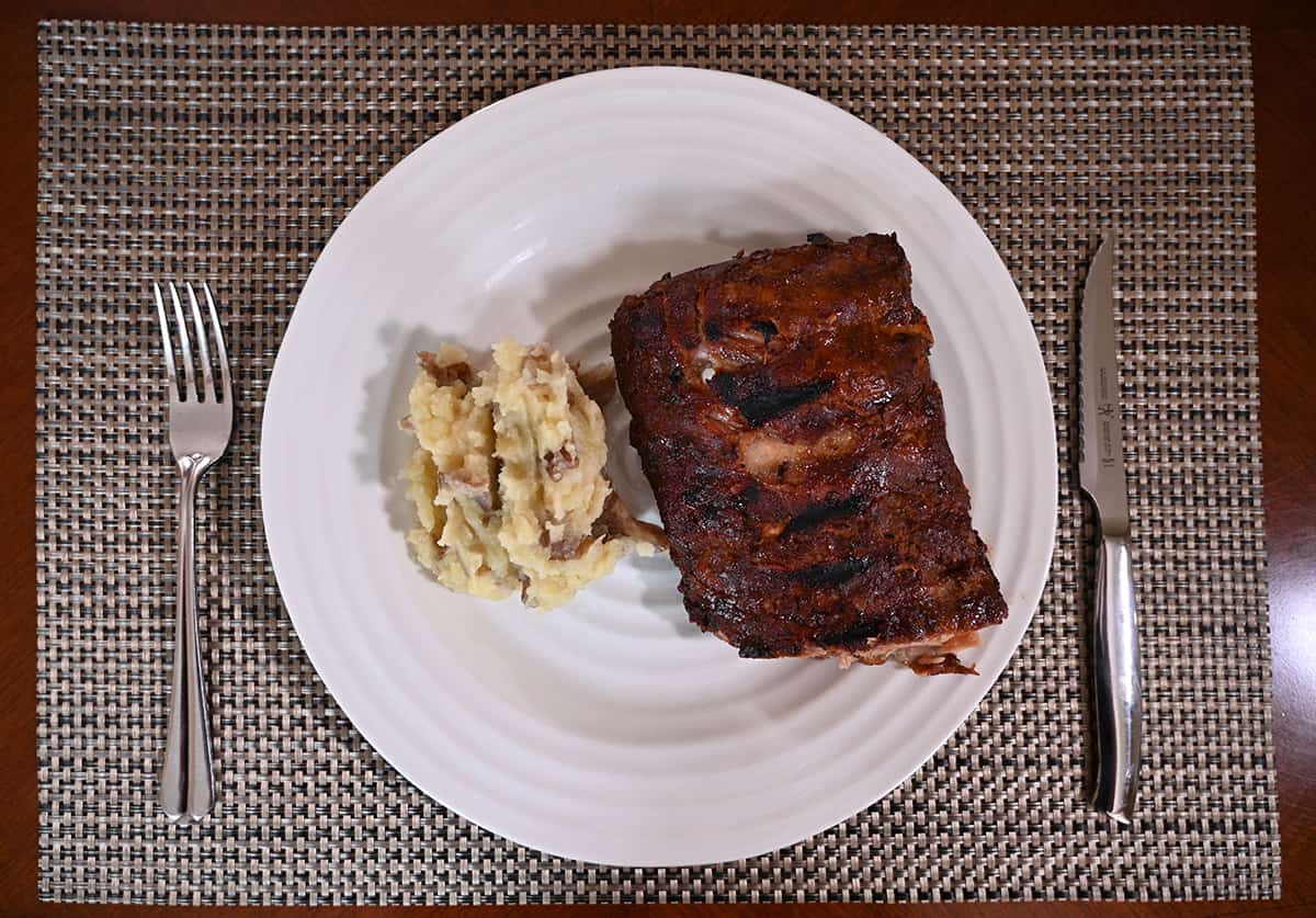 Top down image of a serving of ribs served on a white plate beside a heap of mashed potatoes.