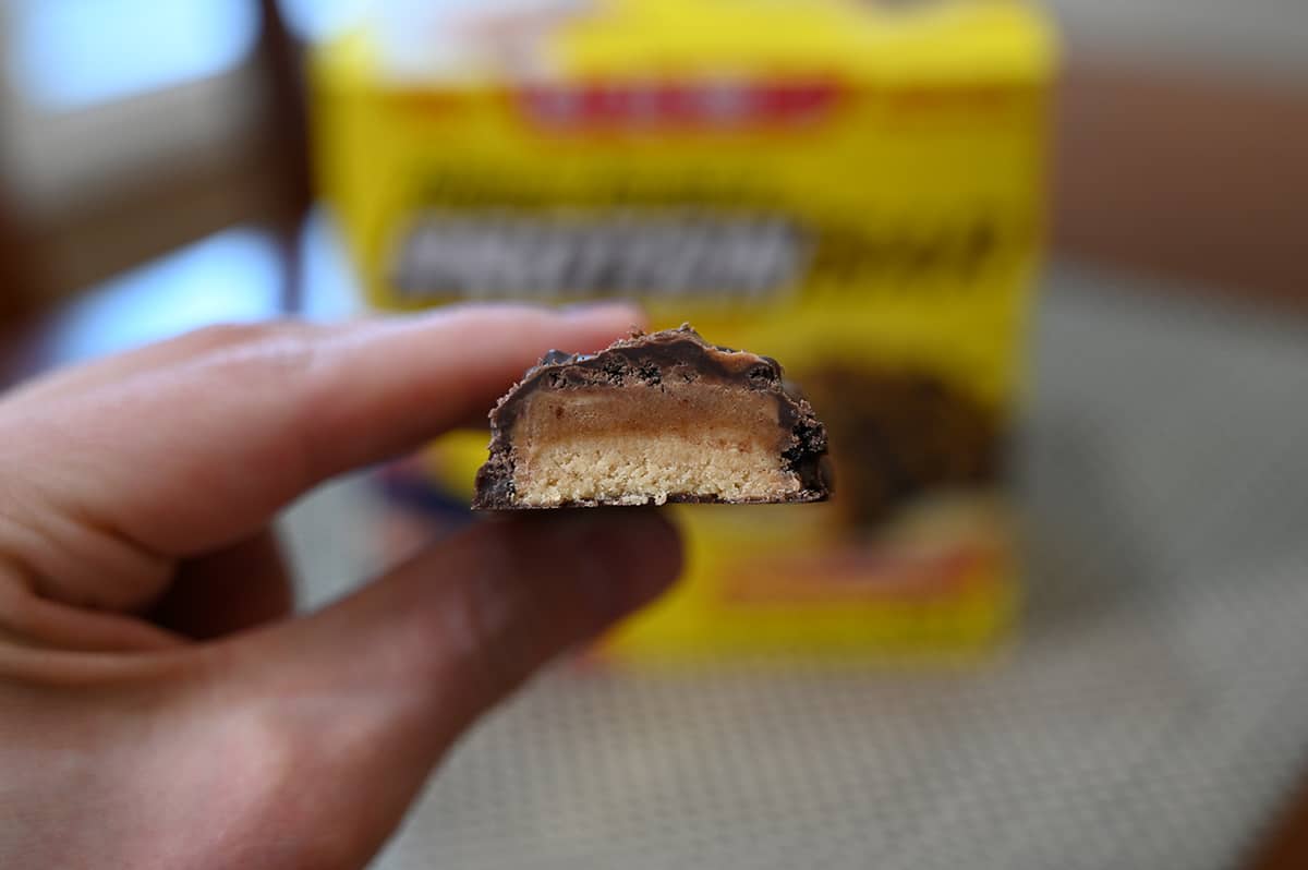 Closeup image of a hand holding a protein bar with a bite taken out of it so you can see the inside and all the layers.