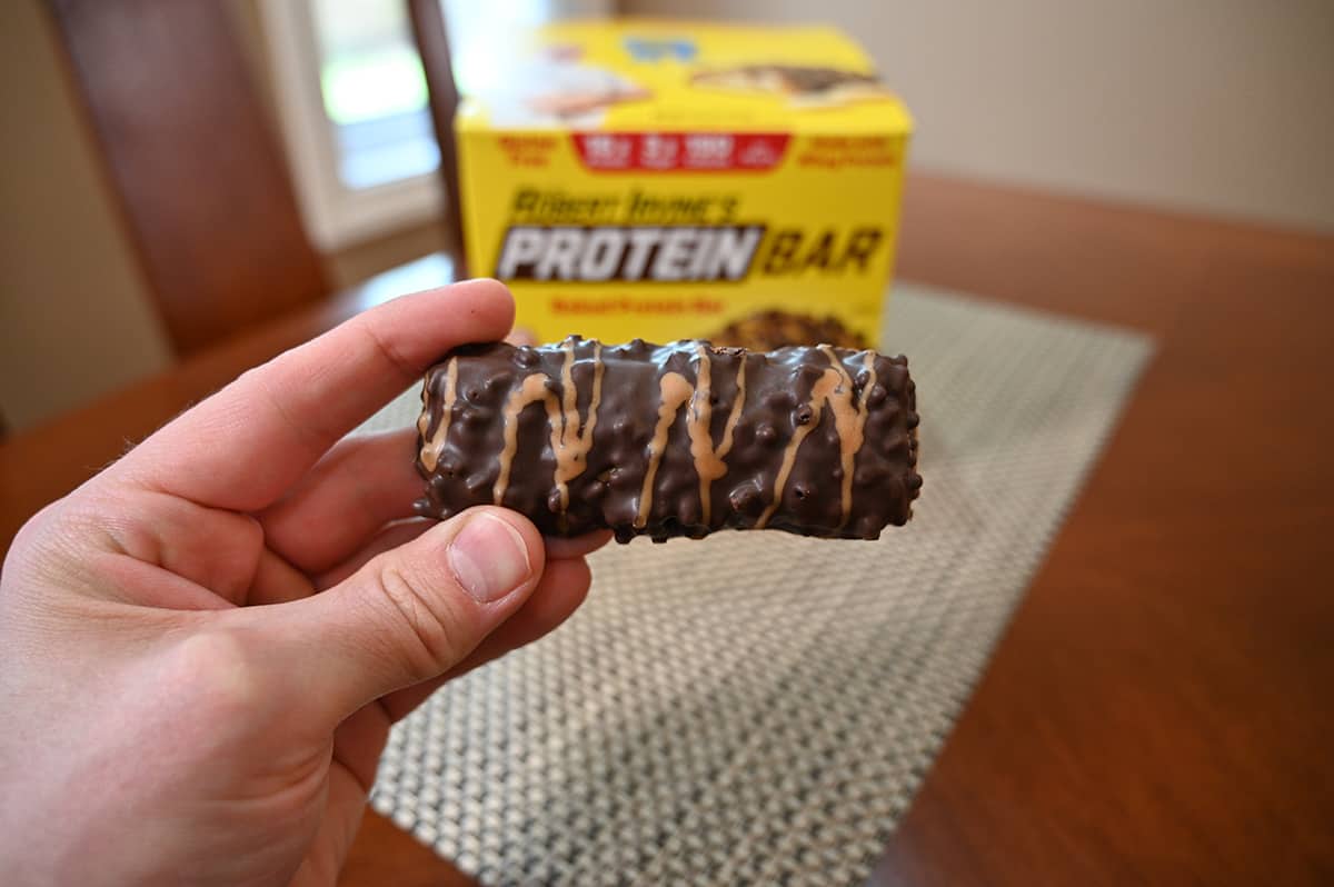 Closeup image of a hand holding one protein bar unwrapped close to the camera.