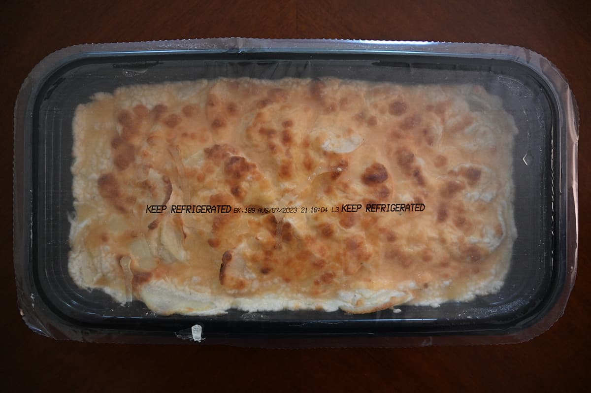 Top down image of scalloped potatoes in a tray, unopened with clear plastic wrap on top.