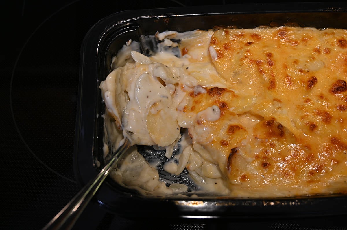 Top down image of a spoon scooping scalloped potatoes out of a tray.