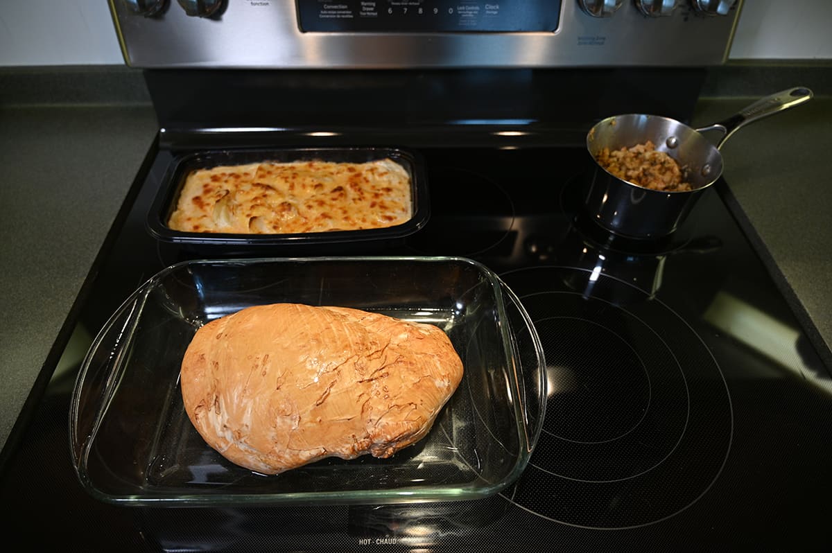 Image of a tray of cooked scalloped potatoes sitting on an oven beside a roast turkey breast and pot of stuffing.