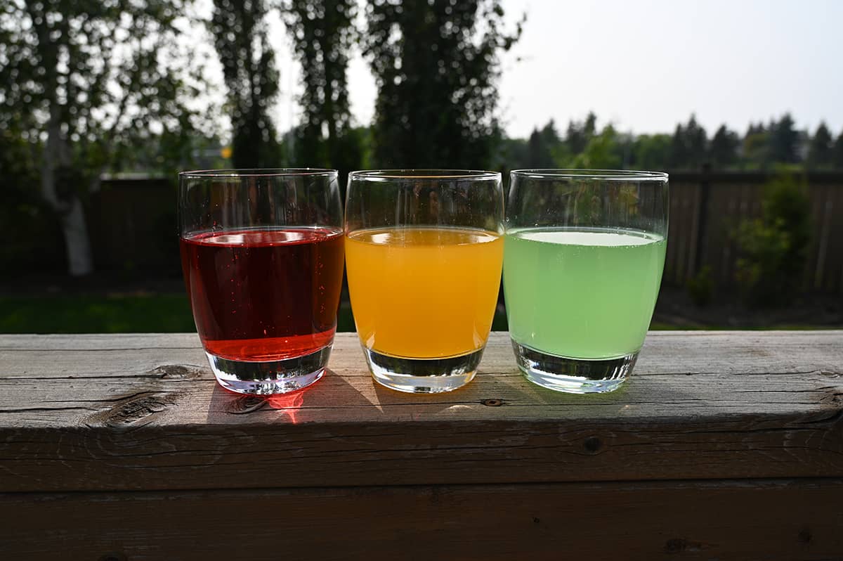Image showing three clear glasses with bottled sparkling water in each glass, the sparkling water is pink, orange and green from left to right.