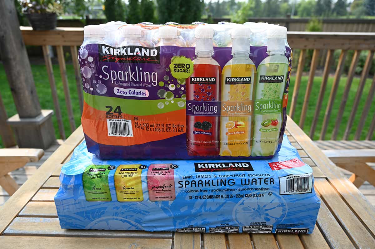 Image of the two cases of Costco Kirkland Signature Sparkling Water sitting on a deck. There's a case of cans and a case of bottles.