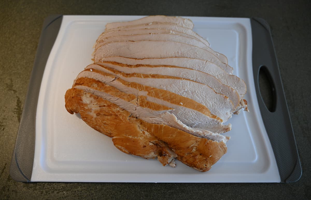 Top down image of a white cutting board with sliced turkey breast on it.